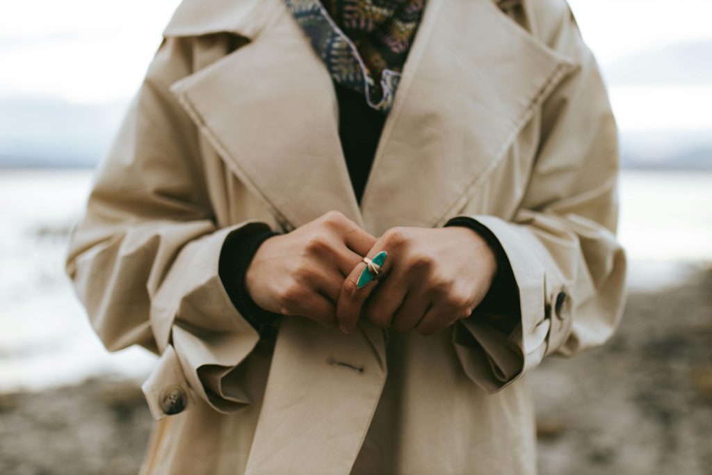 person in trench coat with hands together